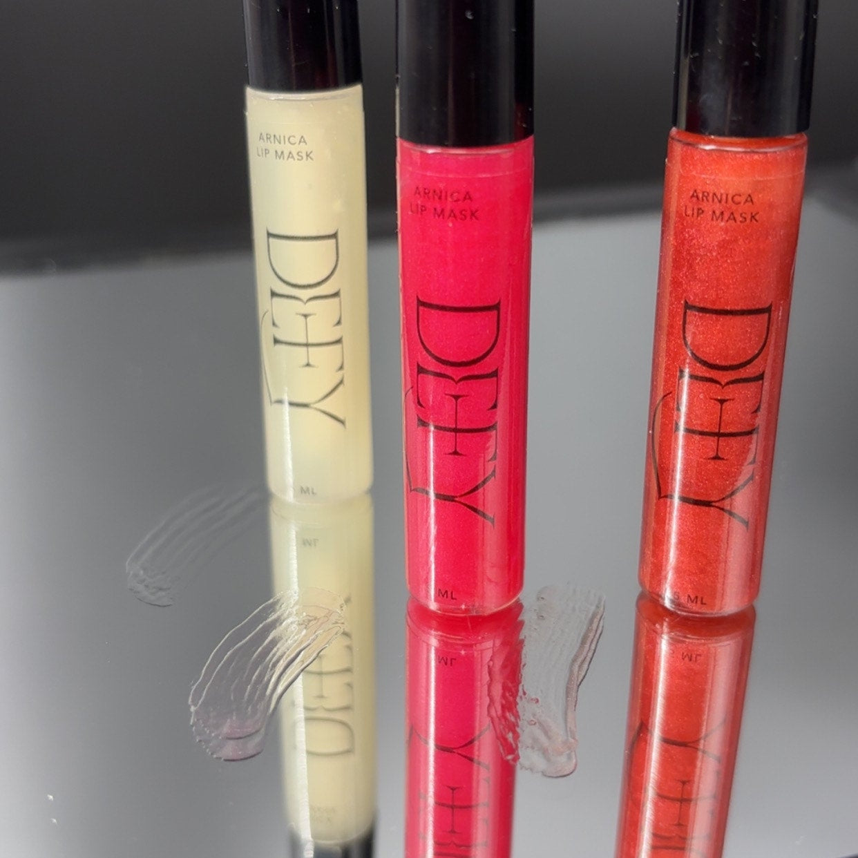 Three lip glosses with black caps on a reflective surface