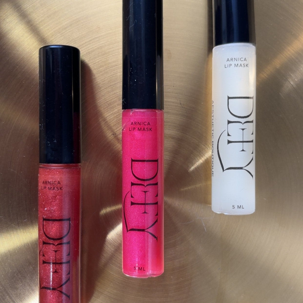 Three lip products with visible brand names on a reflective surface